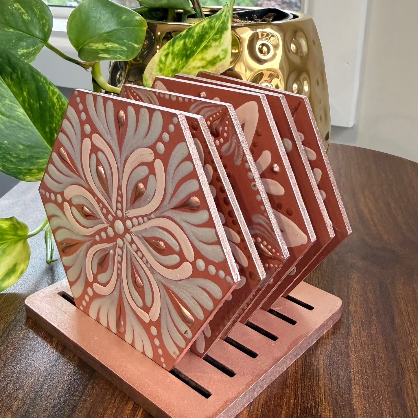 Set of decorative coasters with a holder on a wooden surface with a plant in the background